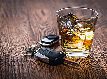 A photo of a filled whiskey tumbler sitting on a table next to car keys.