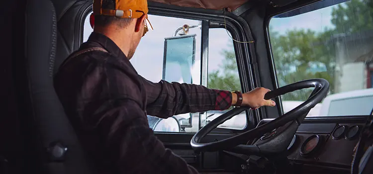 A photo of a truck driver behind the wheel looking out their driver's side window