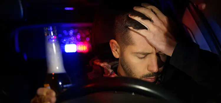 A photo of a male driver pulled over by police while driving with a beer in his hand.