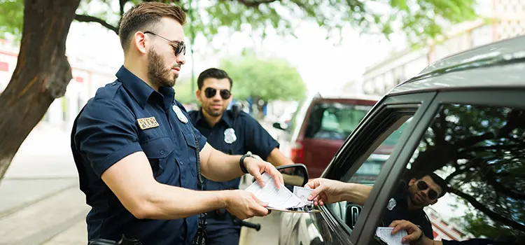 A photo of 2 police officers issuing a ticket to a driver.