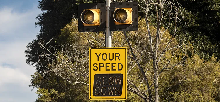 A yellow traffic signal with a digital screen that reads 'Your Speed: Slow Down'.