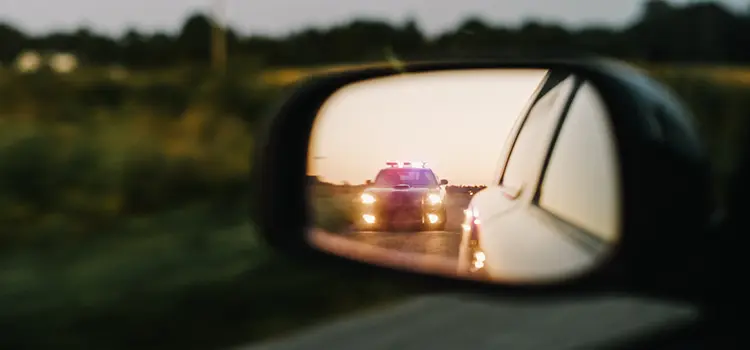 A photo of a police car with its lights on in a driver's mirror.